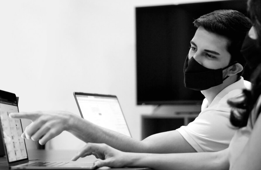 YOUNG DEVELOPER POINTING AT COWORKER'S DESKTOP SCREEN